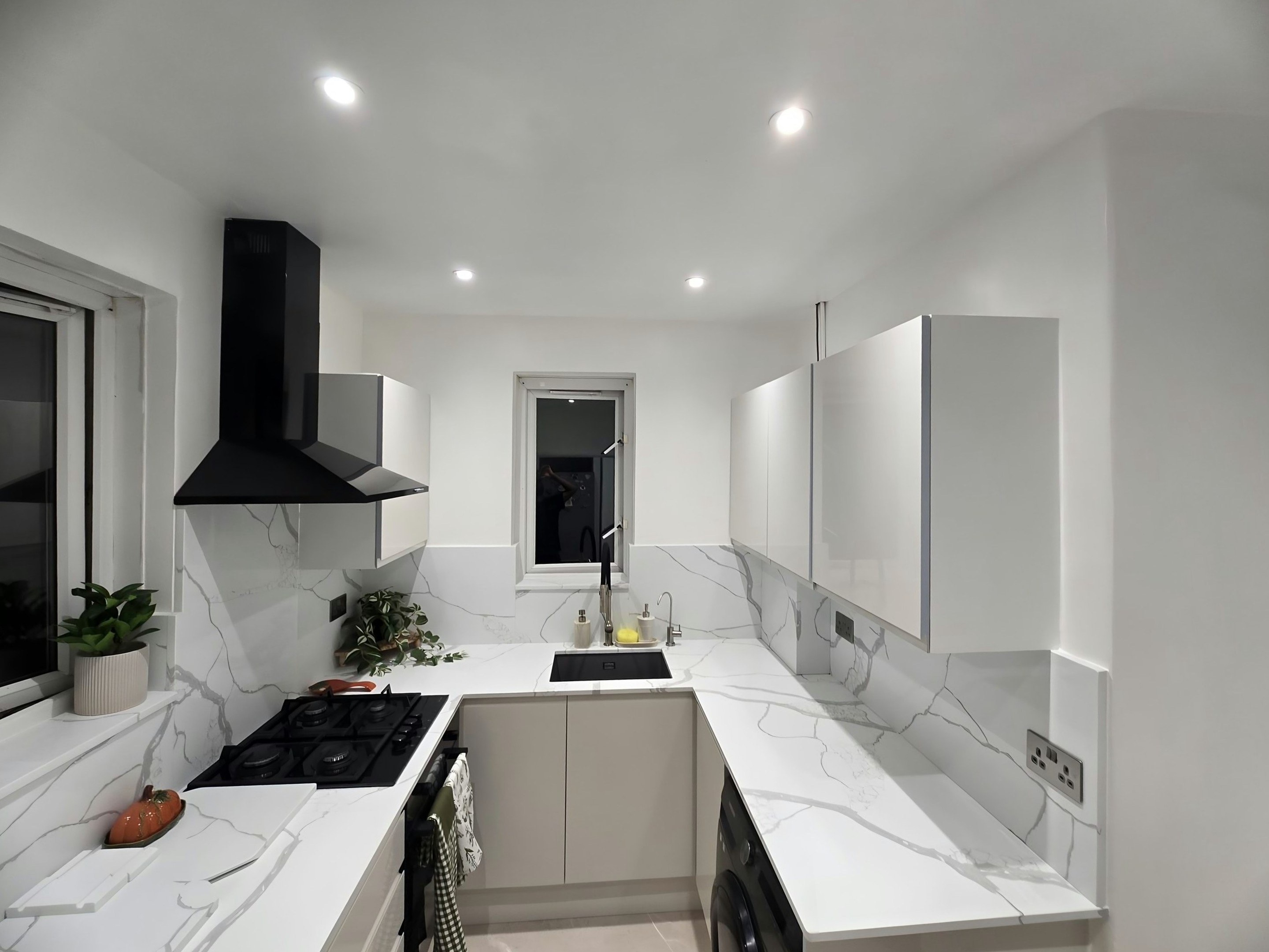 Calacatta Venato worktop and splashback past a black gas hob and chimney extractor to the undermount sink under the window