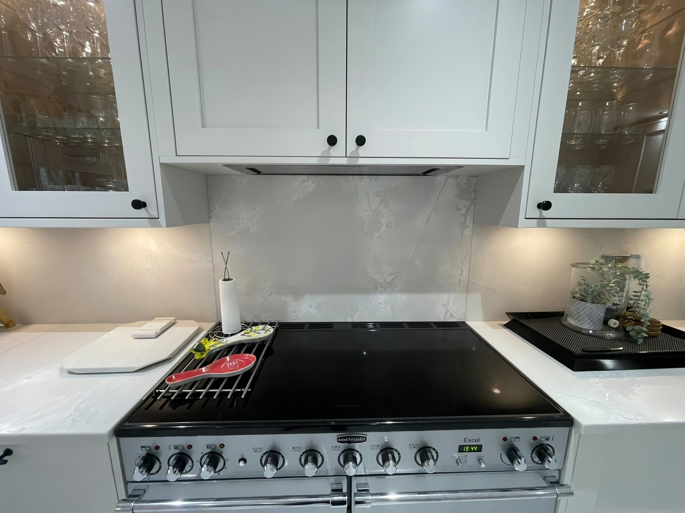Range cooker set between Polar White runs, with a contrasting veined grey splashback carried up the wall behind it