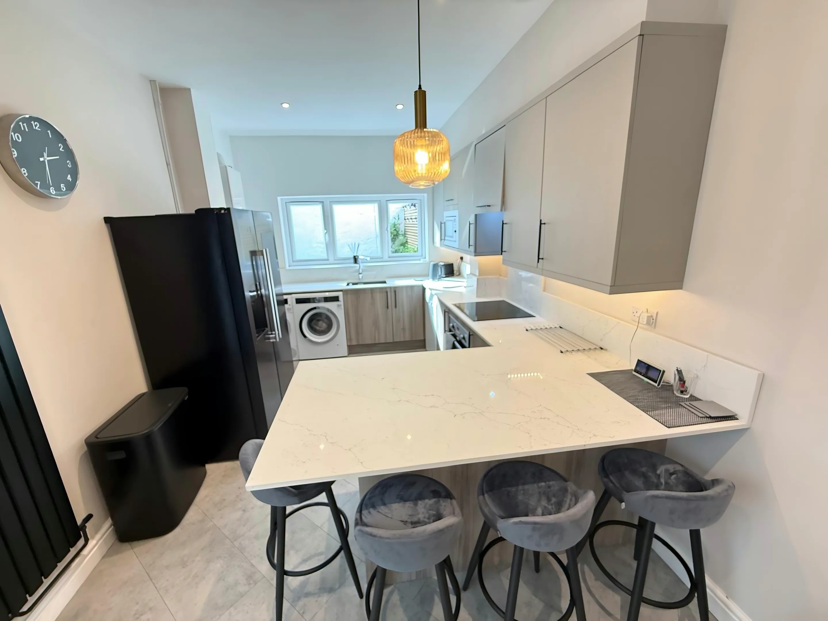 White veined breakfast bar with four grey velvet stools in a pale grey handleless kitchen