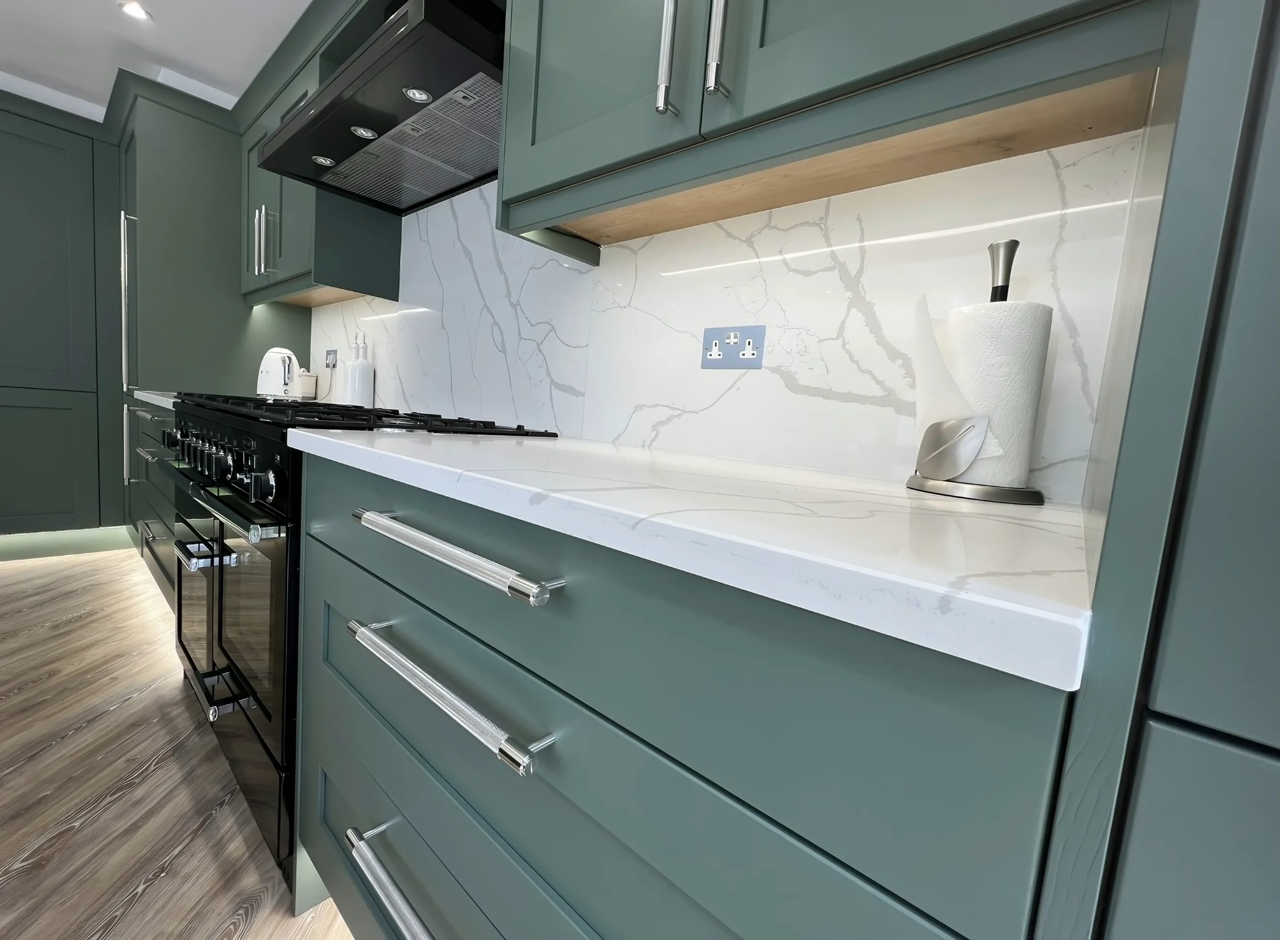 Close view of a polished quartz worktop edge above green shaker drawers